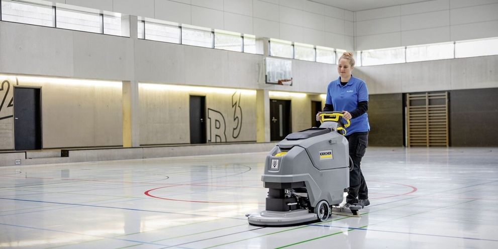The walk-behind scrubber dryer in use A person cleaning the floor in the gym with a scrubber dryer