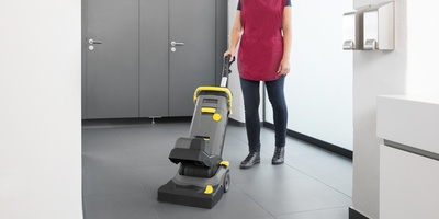 Person cleaning a public bathroom with a scrubber dryer Person cleaning a public bathroom with a scrubber dryer