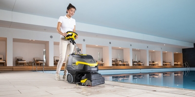 Person cleaning alongside a hotel pool with a scrubber dryer Person cleaning alongside a hotel pool with a scrubber dryer