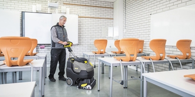Person cleaning a class room with a scrubber dryer