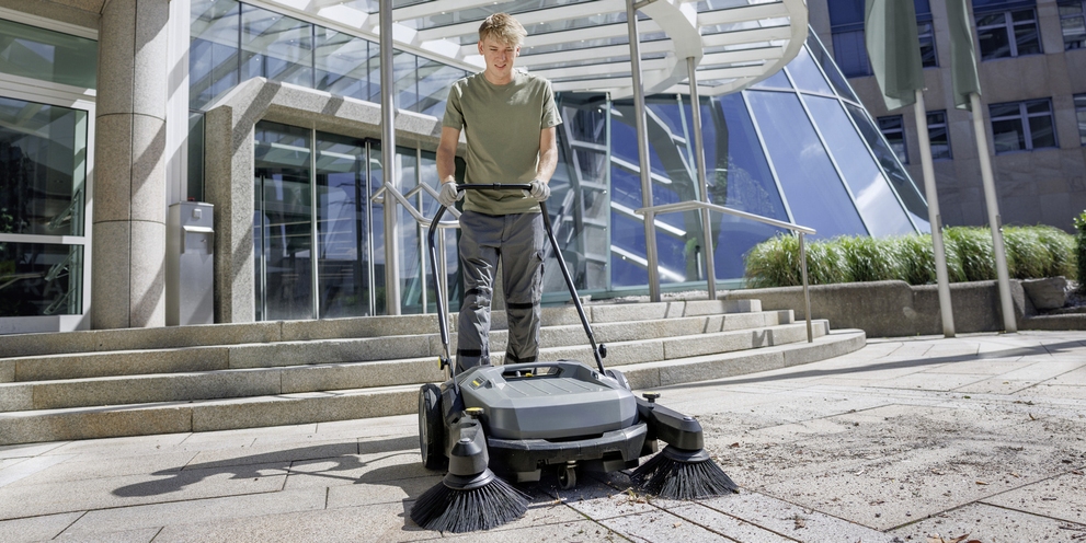 A person cleaning the forecourt of a hotel with a Kärcher sweeper
