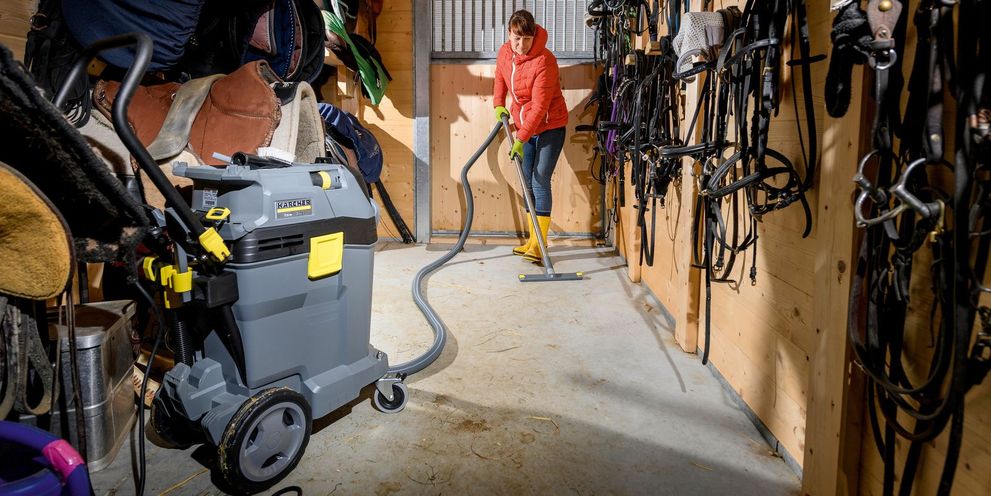 A woman cleans a tack room with a Kärcher wet/dry vaccum cleaner