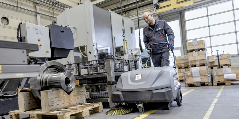 A man cleans the floor with a walk-behind sweeper