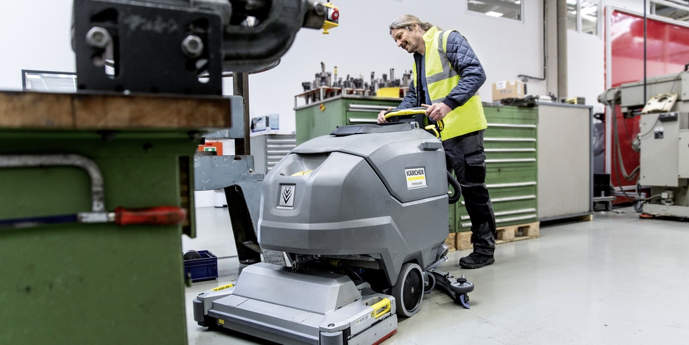 A man cleans the floor with the walk-behind scrubber-dryer