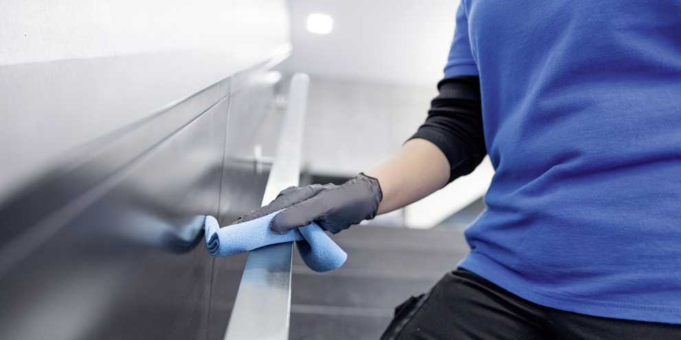 A person cleans a handrail with a microfiber cloth
