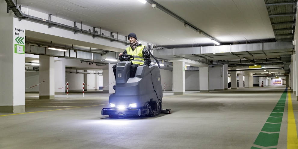 A person is cleaning an underground parking garage with a Kärcher ride-on scrubber dryer