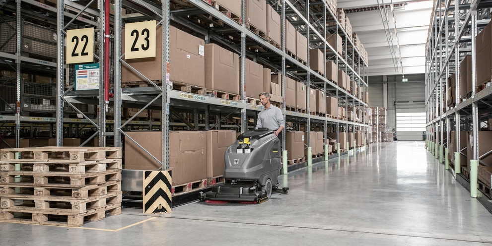 Cleaning in logistics A person cleans a warehouse with a Kärcher sweeper