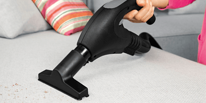 The hand nozzle of the Kärcher SV 7 with upholstery attachment cleans a grey sofa deep into the fibres.