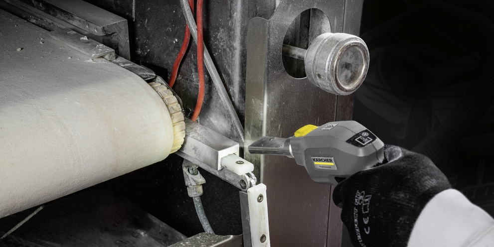 A transport belt is cleaned with a dry ice blaster