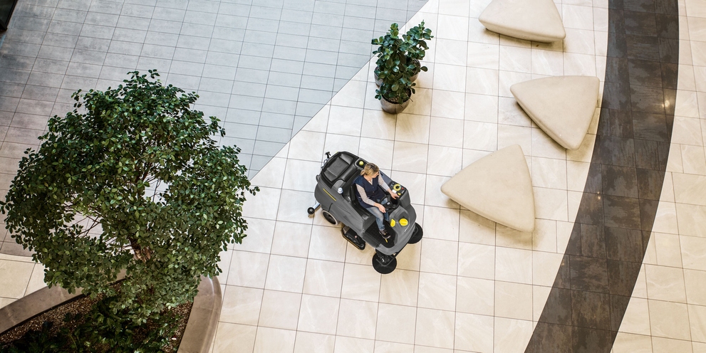 The ride-on scrubber dryer in use A person cleaning the extensive floor with a Kärcher ride-on scrubber dryer