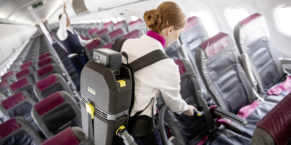 A person cleaning the seating of an airplane with a backpack vacuum cleaner