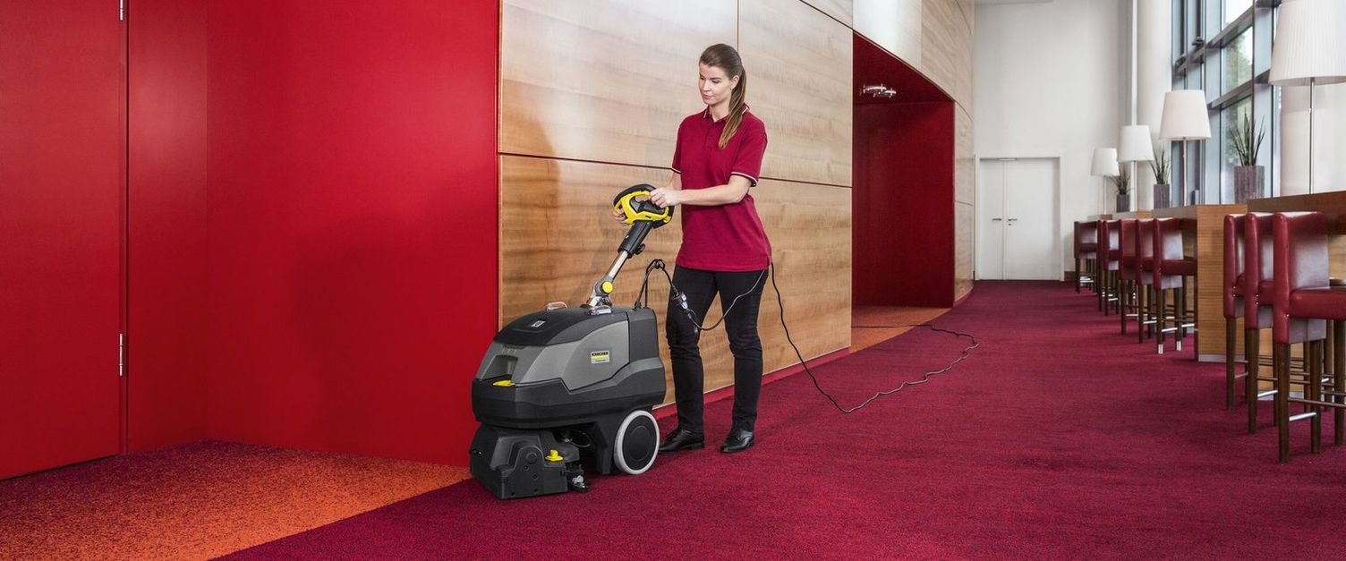 A woman cleans a red carpet with a Kärcher handheld vacuum sweeper