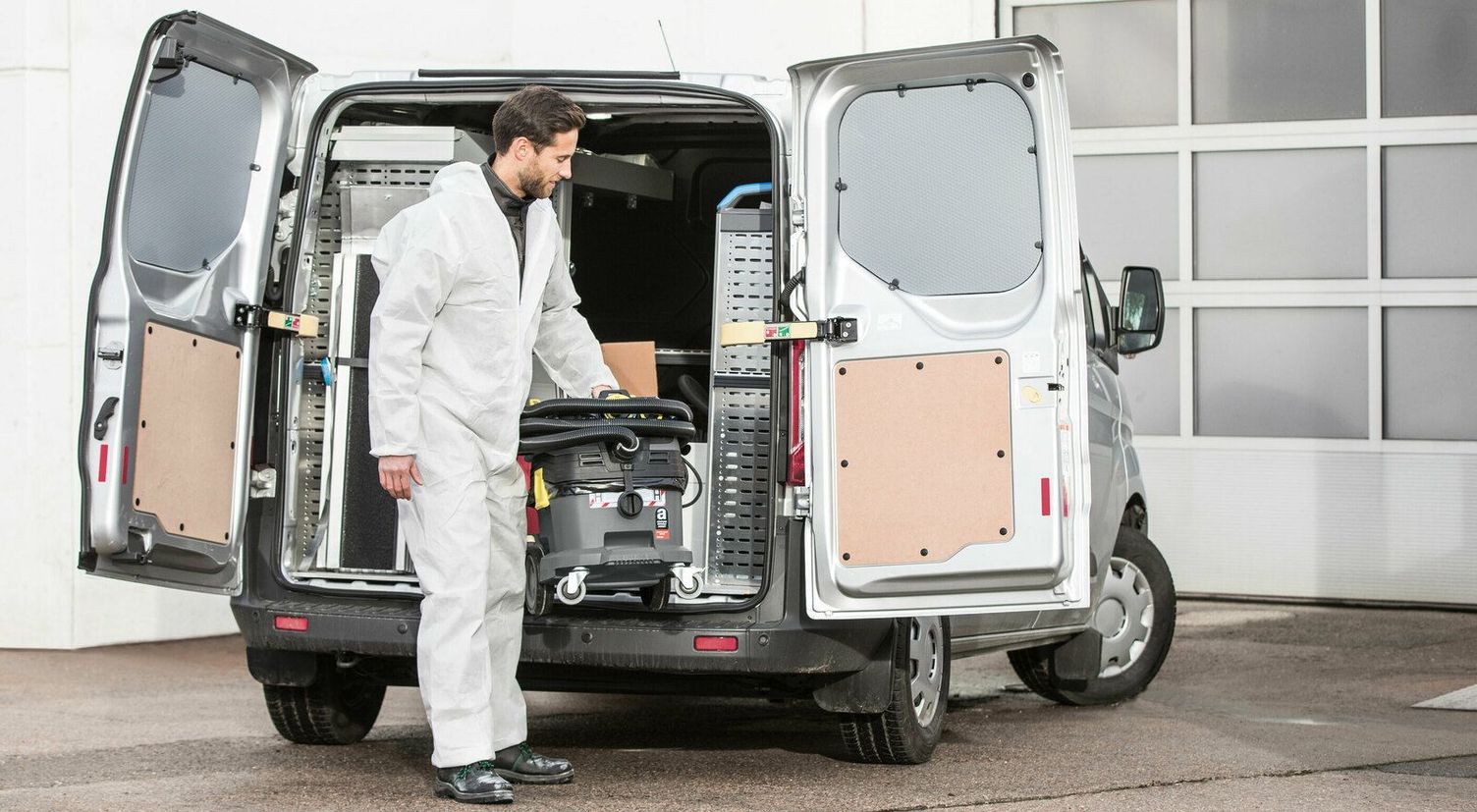Asbestos disposal A person in a white protective suit takes a Kärcher Wet and Dry Vacuum Cleaner out of the van