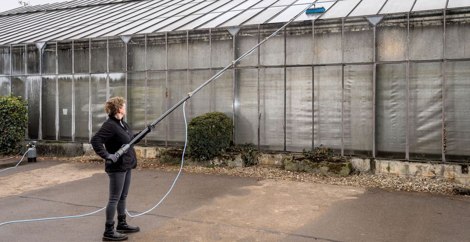 A woman cleans the outside of a greenhouse with a Kärcher telescopic lance