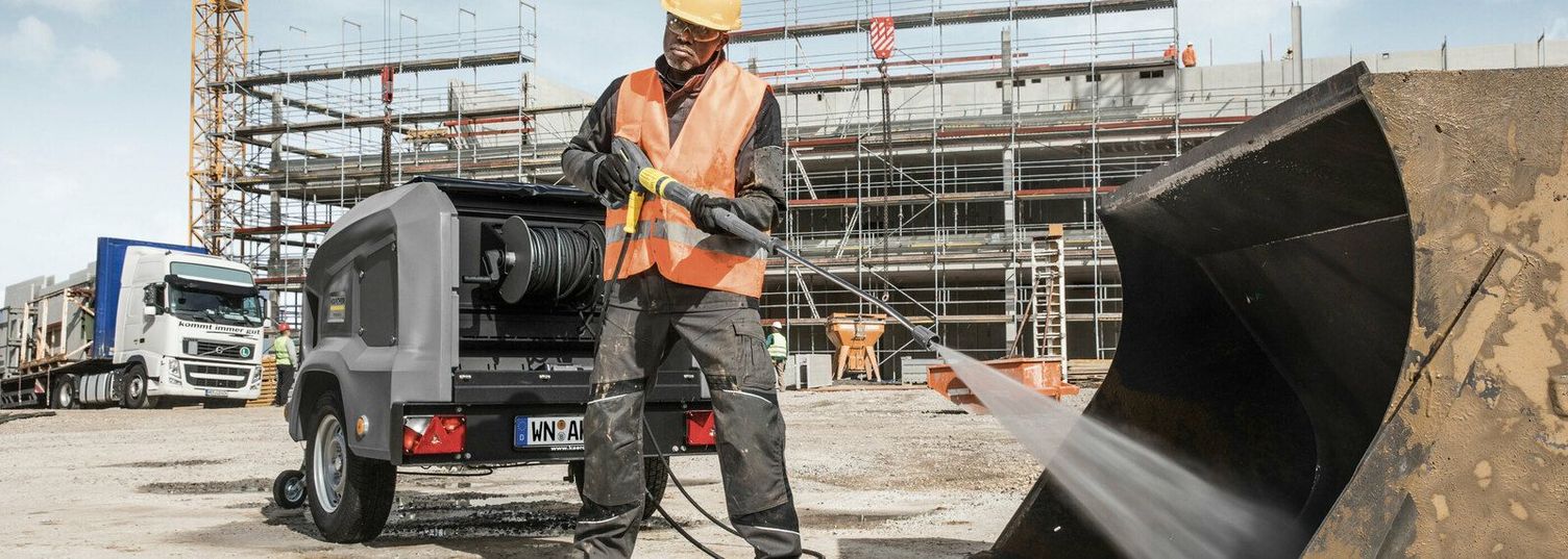 A person cleans an excavator bucket with a Kärcher Hot Water High-Pressure Trailer