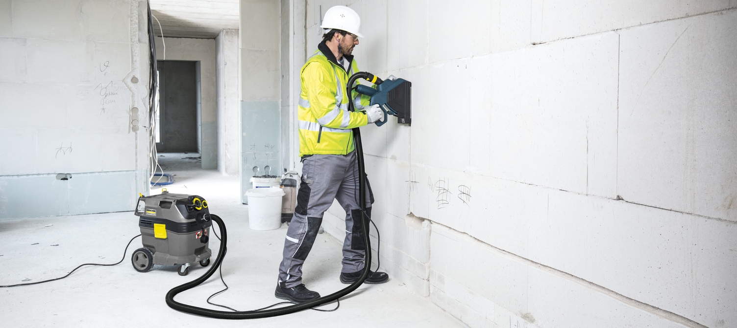Person vacuuming dust from a wall on a construction site