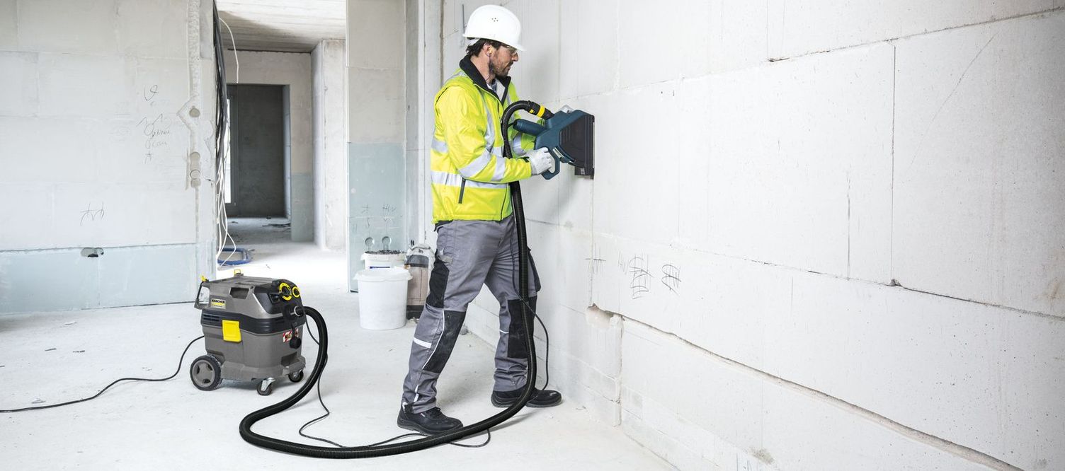 A person in work clothes is vacuuming dust on a construction wall