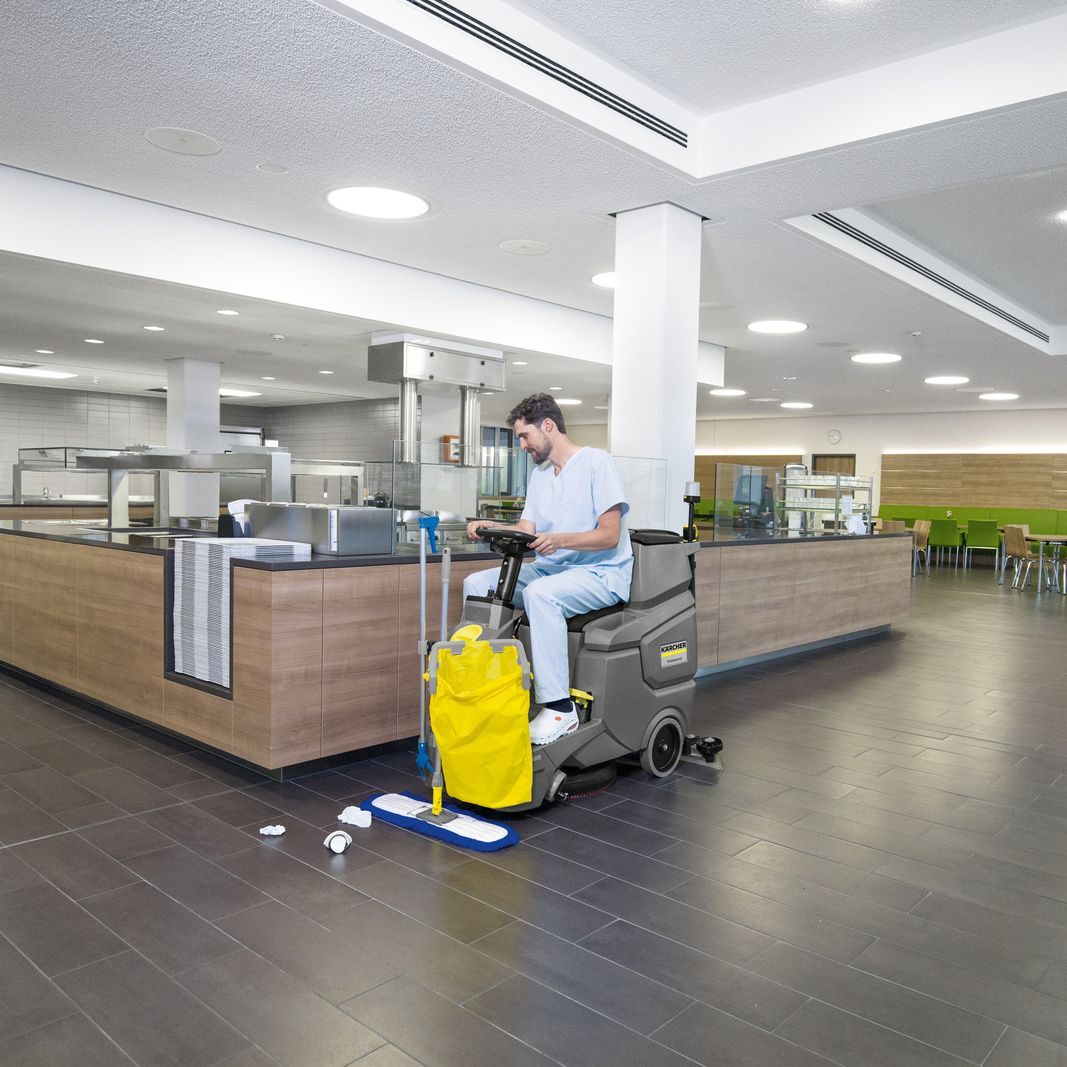 Man seen on a Kärcher ride-on scrubber dryer in a canteen