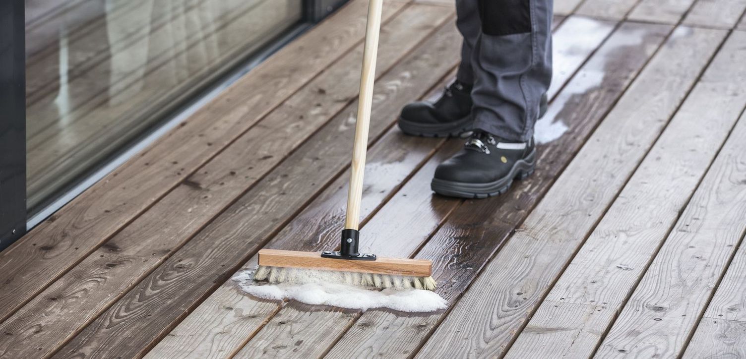 Using a broom to spread a liquid on a wooden deck