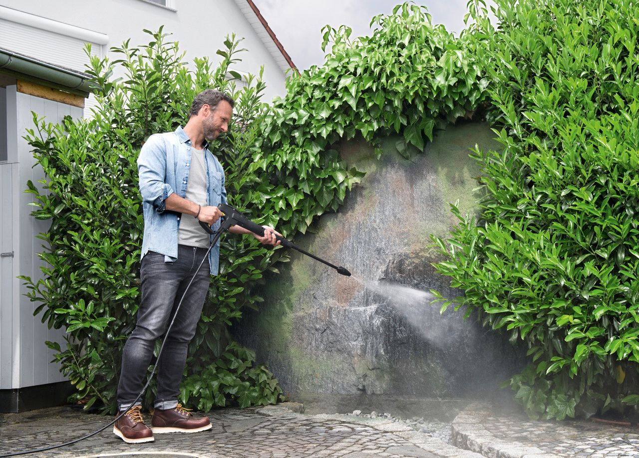 A man removes moss on a wall with a Kärcher pressure washer