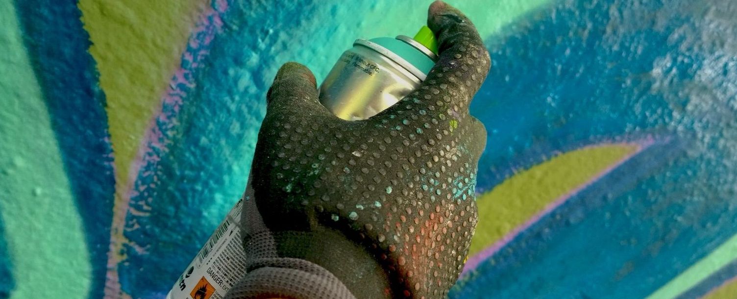 A hand in a glove sprays paint on a wall with a graffiti can