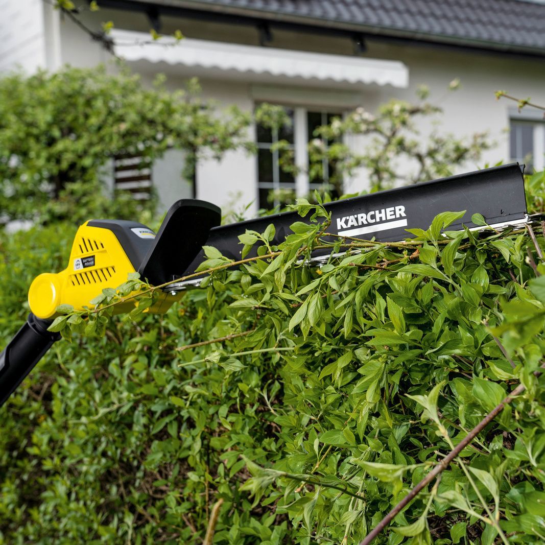 The Kärcher battery hedge trimmer with hedge broom in use on a hedge