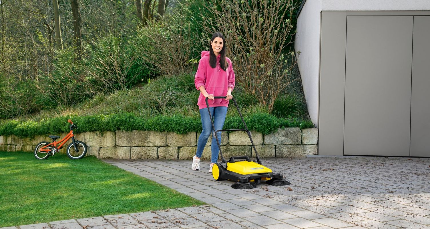 A woman cleans her garage driveway with a Kärcher sweeper