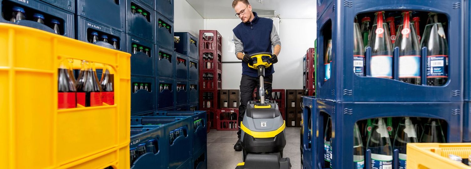 Cleaning a filled cold room with a scrubber dryer Front view of a man cleaning between crates of drinks with a cleaning machine.