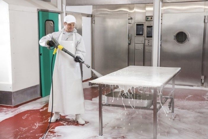 A man in white work clothes cleans a table top using a Kärcher high-pressure washer