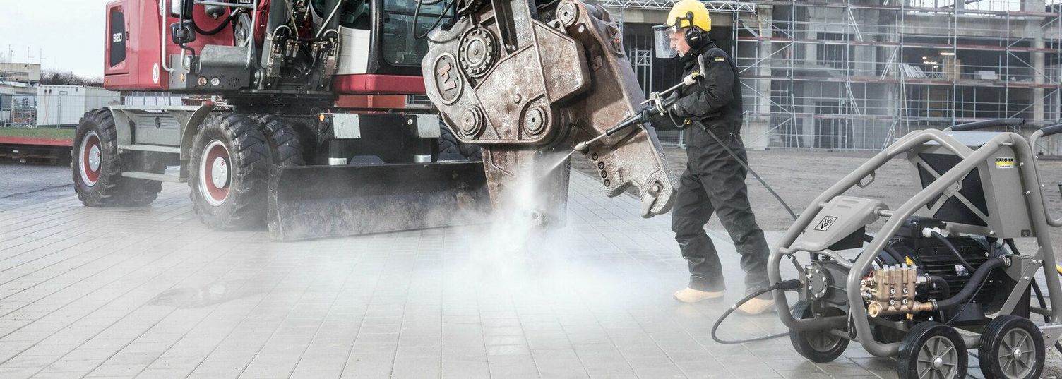 Cleaning construction equipment A person in protective clothing cleans a red machine with a Kärcher Ultra-High-Pressure Cleaner