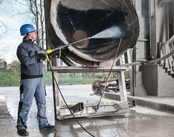 A person wearing protective clothing cleans a concrete mixer with a Kärcher High-Pressure Cleaner