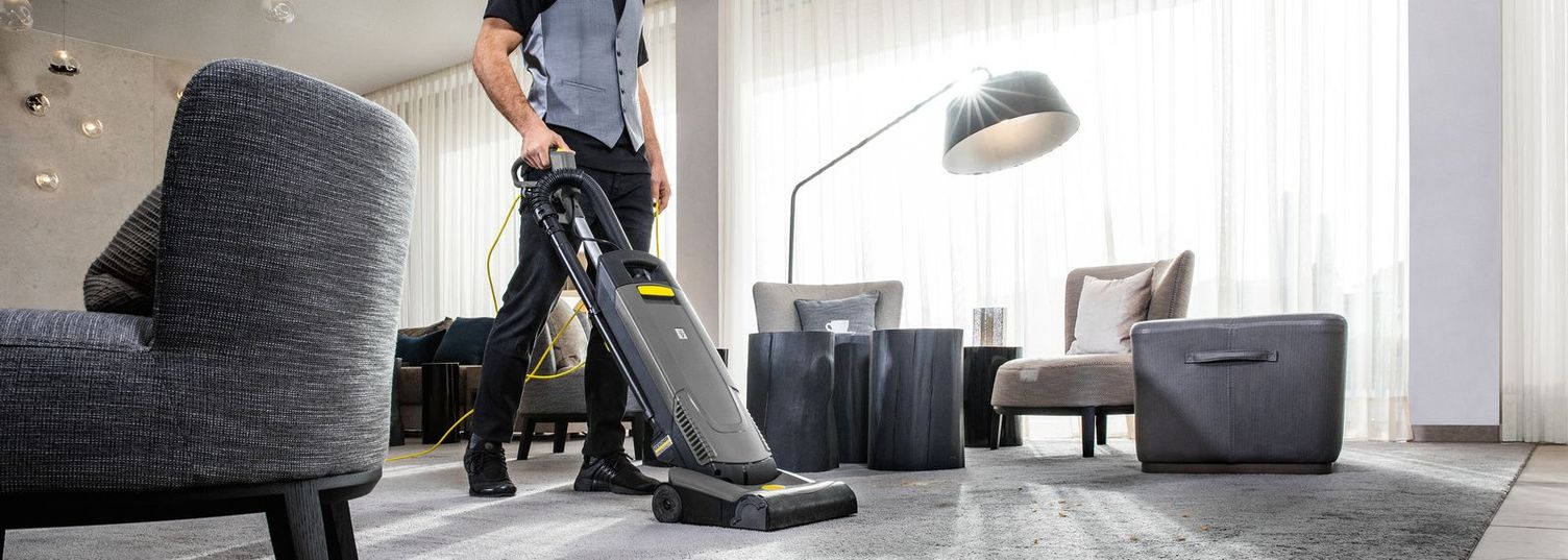 A woman cleans the carpet in a hotel room with a Kärcher device