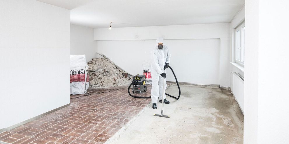 A person in white protective clothing cleans residues on the floor of a renovated apartment using a Kärcher Vacuum Cleaner
