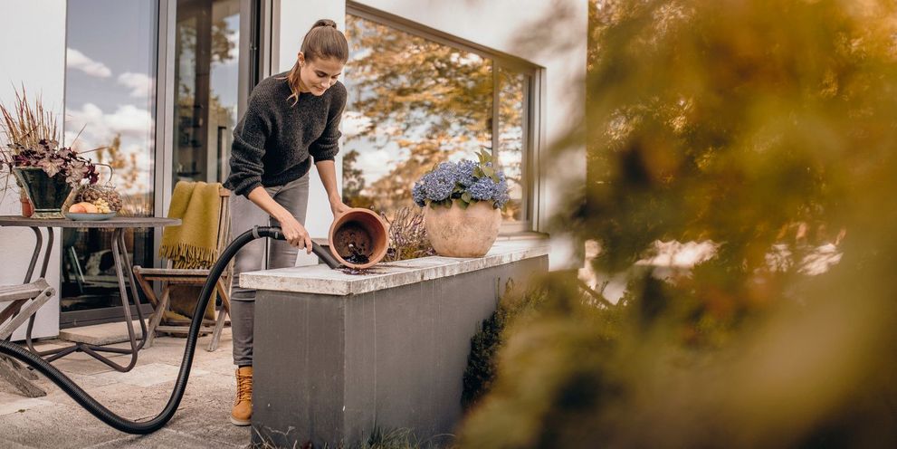 A woman removes soil from her flower pots with a Kärcher wet and dry vacuum cleaner