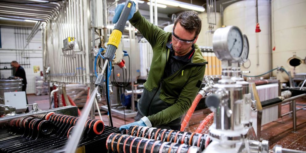 A man cleans a wine bottling machine with a Kärcher high-pressure cleaner