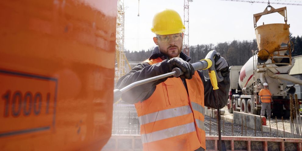 A person wearing a high-vis vest cleans a construction tank using a Kärcher Ultra-High-Pressure-Cleaner