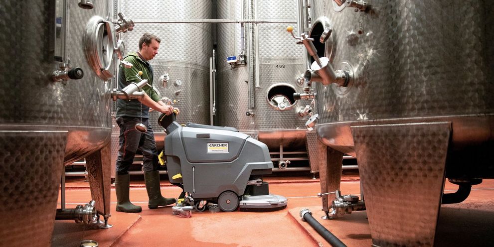 A man cleans the floor in the wine cellar with a Kärcher scrubber dryer