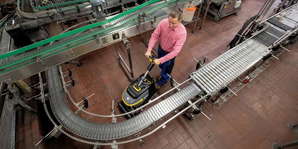 View from above: a man cleans the floor around a bottling line with a Kärcher floor cleaner