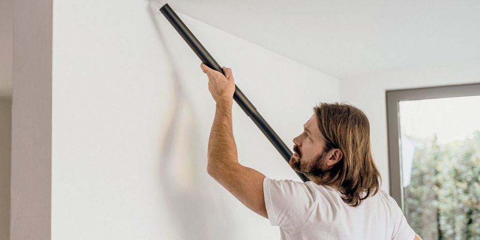 A man vacuums the ceiling of a flat with an extension add-on