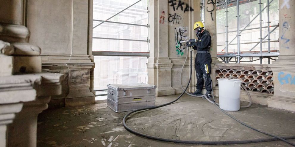A person in protective clothing removes graffiti from the inside of a house wall