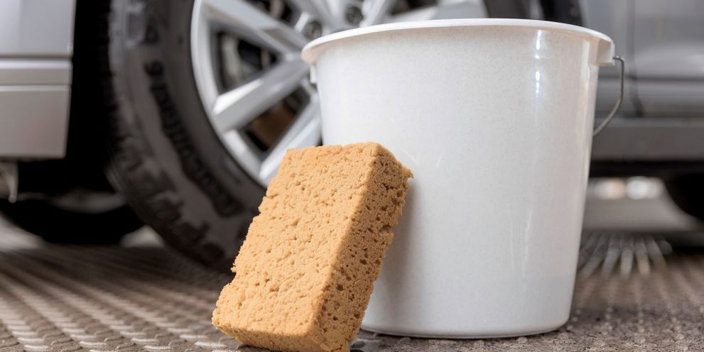 Bucket of homemade cleaner and sponge in front of a rim