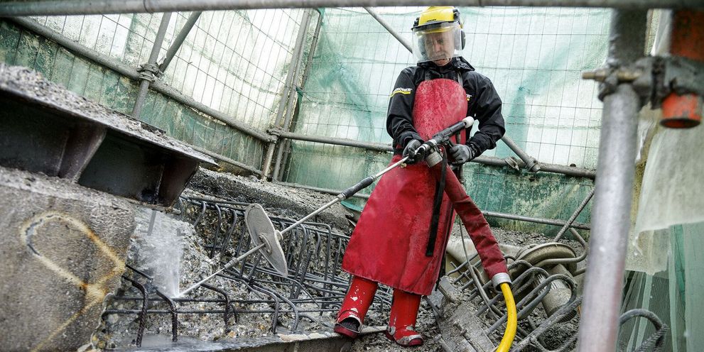 A person in protective clothing uses a Kärcher Ultra-High-Pressure Cleaner to clean concrete construction debris