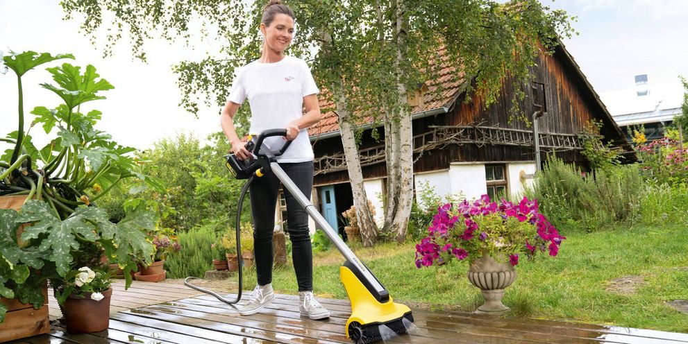 A woman cleans her wooden decking with a Kärcher patio cleaner