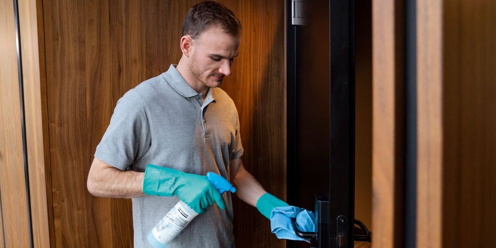 A man disinfects the door handle of a hotel room