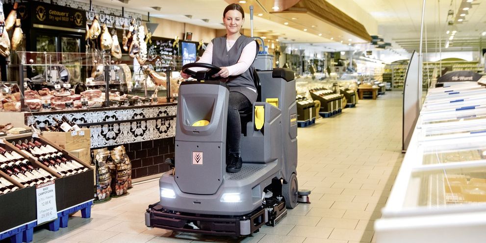 A person sits on a Kärcher sweeper machine cleaning the floor of a supermarket