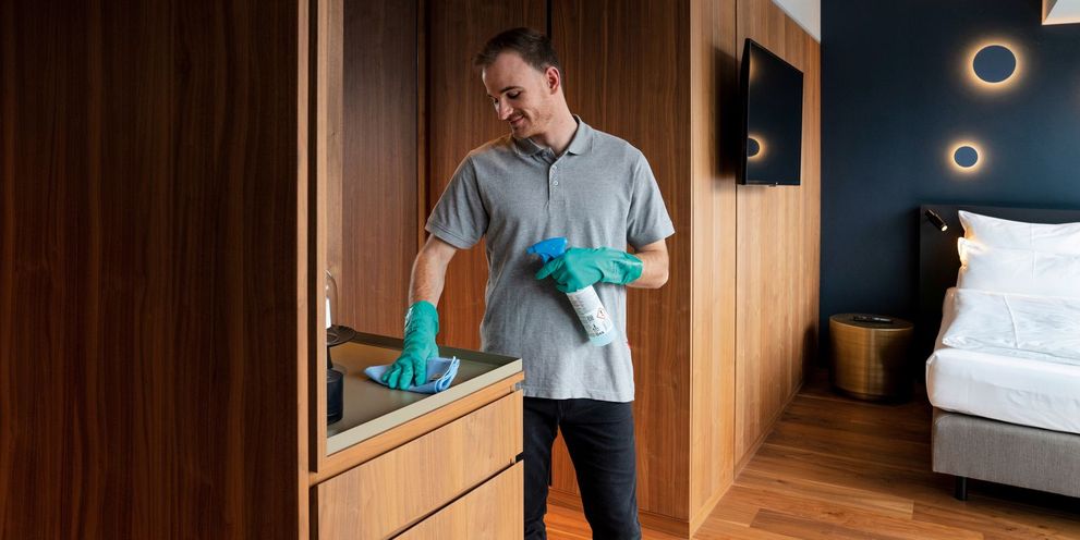 A man manually cleans the furniture in the hotel room
