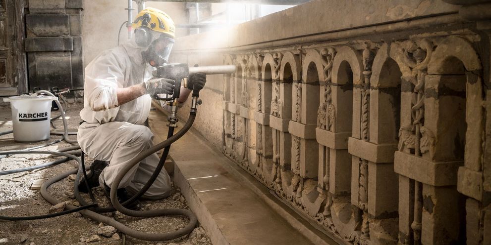 Monument cleaning with a low-pressure particle blasting method A person cleans a wall with a jet gun