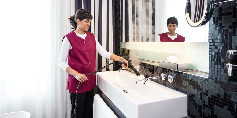 A woman cleans a sink in a hotel room with a Kärcher steam cleaner
