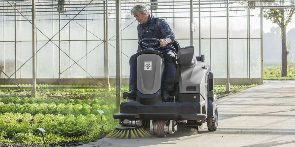 A man cleans the floor of a greenhouse with a Kärcher ride-on sweeper vacuum cleaner