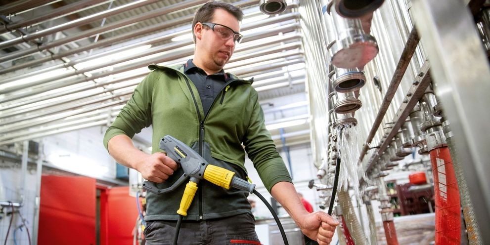 A man cleans piping on a wine bottling machine with a Kärcher high-pressure cleaner